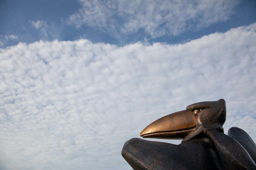 a Jayhawk statue against a blue sky with white clouds