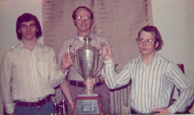 three men hold up a large trophy