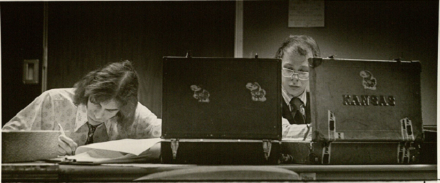 two debate team members prepare at a desk with briefcases