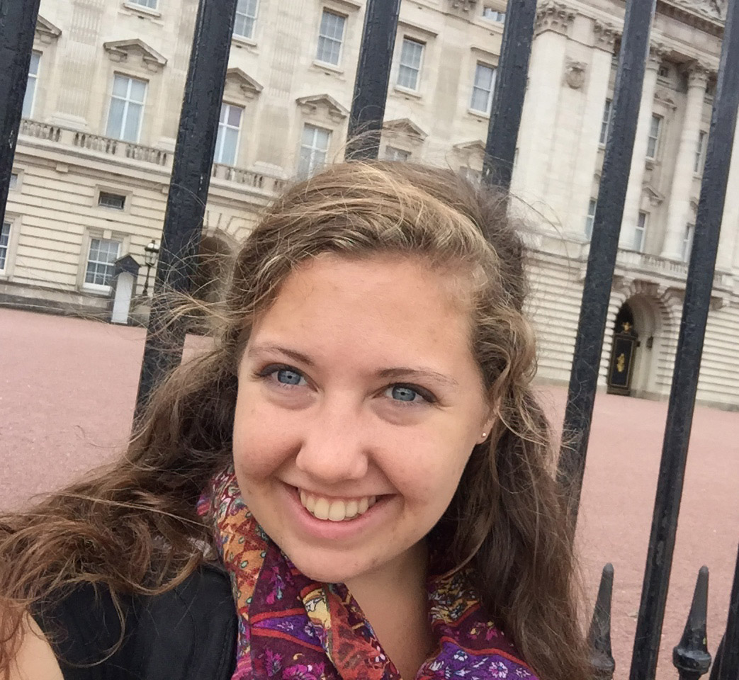 Kathleen Meeds in front of a wrought iron fence with a large building behind it