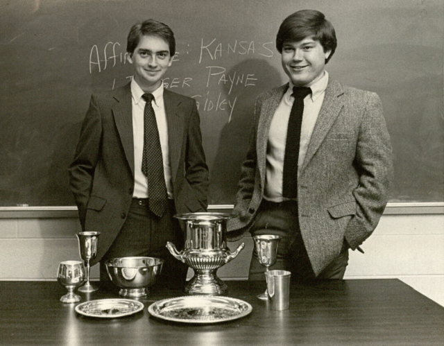 Mark Gidley and Rodger Payne in front of a classroom with champion trophies