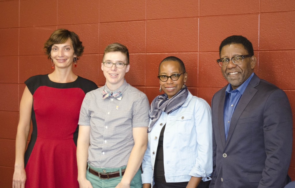 A group of four people stand in front of a red wall