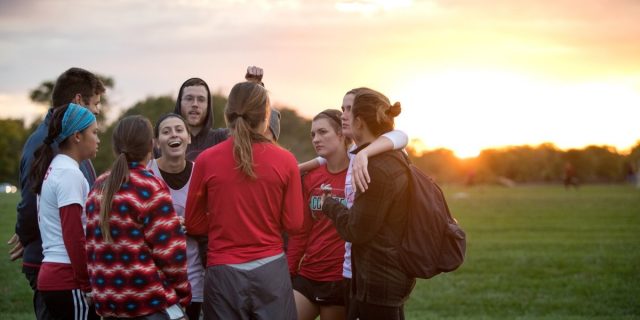 An image of 9 KU students standing in circle, talking, laughing and hugging as the sun sets in the background. 