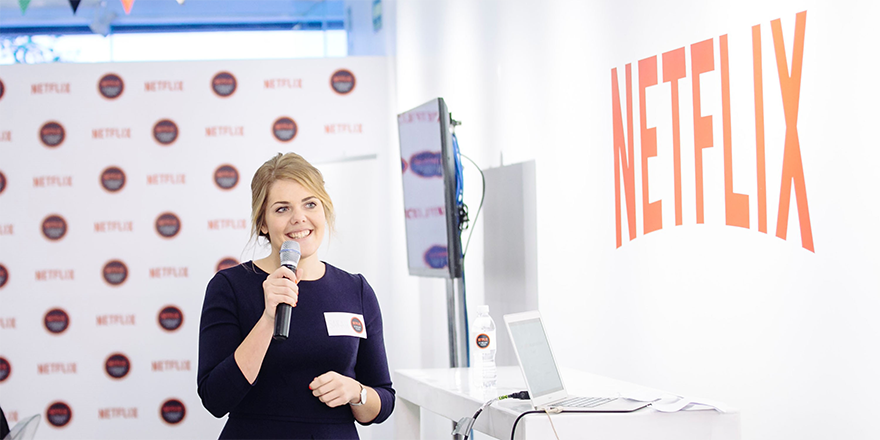 Sarah Stern holding a microphone in front of a sign that says Netflix