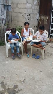 three children sitting down eating boxed meals