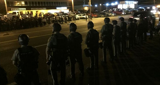 police officers in riot gear lined up across a street from protesters