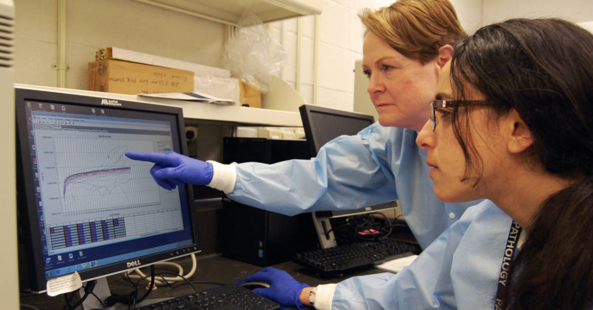 Two people look at a computer screen with a graph on it