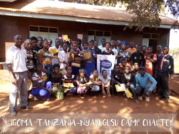 A group of people in front of a building with the text 'Kigoma Tanzania-Nyarugusu Chapter'