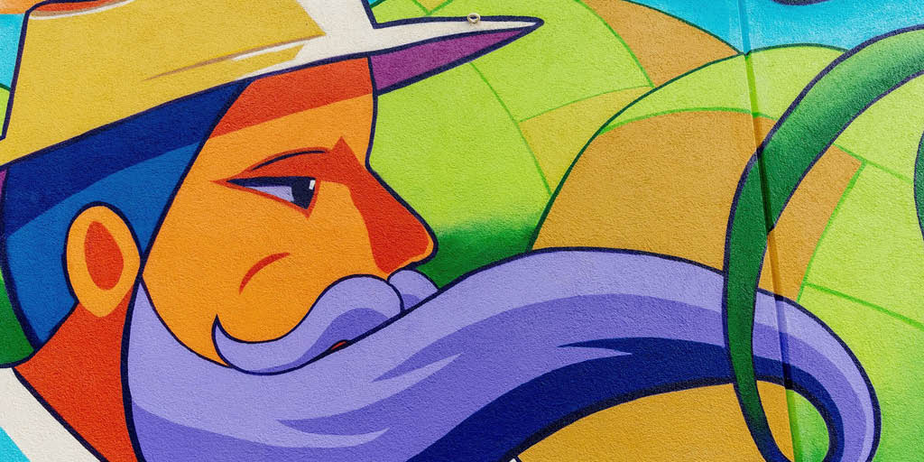 Colorful mural of a character with a long purple mustache, wearing a yellow hat, against a background of green and blue geometric shapes.