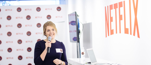 Sarah Stern holding a microphone in front of a sign that says Netflix