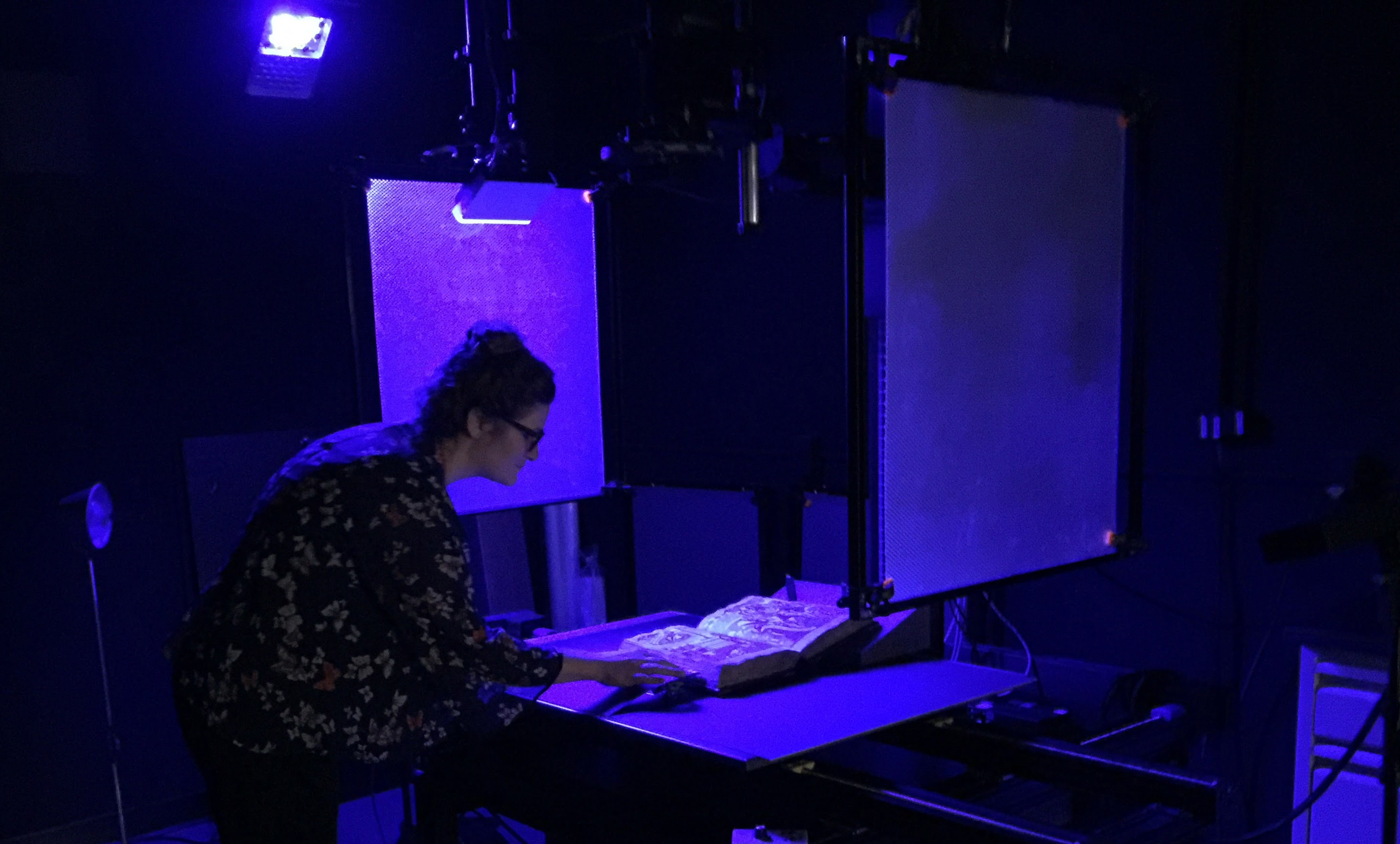 Stephanie working on an old book in a dark room with purple UV light. 
